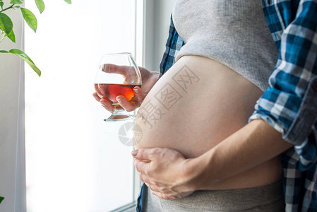 孕妇在窗户边大肚子的怀孕妇女拿着一杯威士忌图片