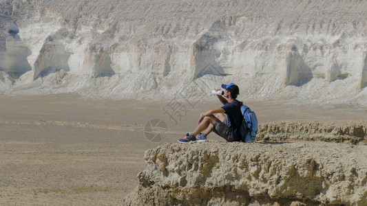 年轻旅行者在岩石上喝水图片