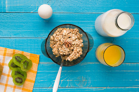 燕麦片加牛奶和猕猴桃碗用勺子在蓝色木制背景上早餐的健康食品顶视图片