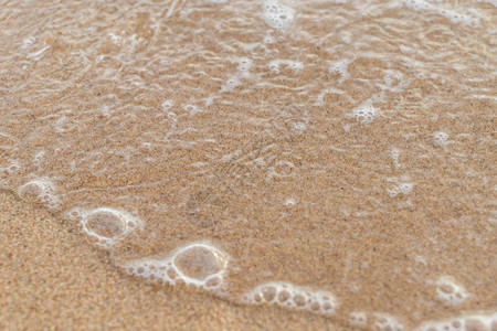 棕色沙滩上带气泡的海水波图片