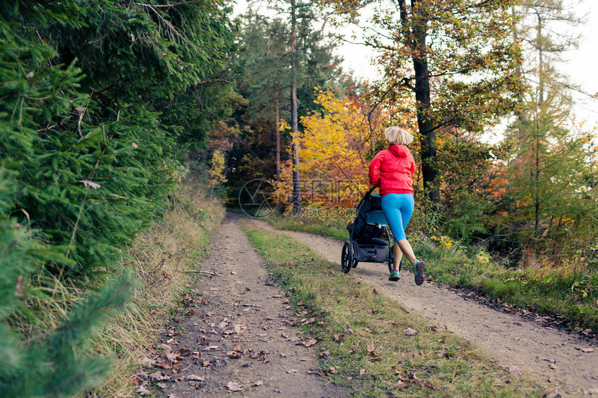 正在运行的母亲带着孩子在秋日的落和山景中享受母婴儿车带着婴儿车在树林里慢跑或行走的女人美图片