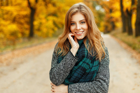 美丽的年轻美女笑着享受秋天的气在黄色树叶附近的图片
