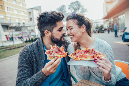 夫妇吃比萨饼在户外和微笑他们在一家户外咖啡馆里分享比萨饼图片