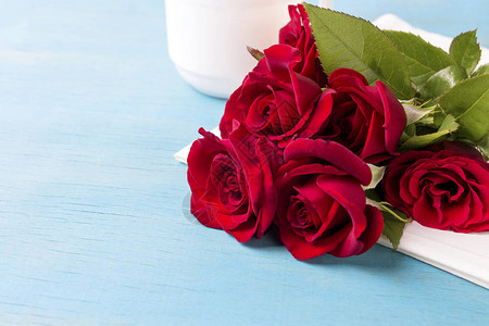 白色餐巾纸和蓝色木制背景上的红玫瑰花束复制空间情人节假图片