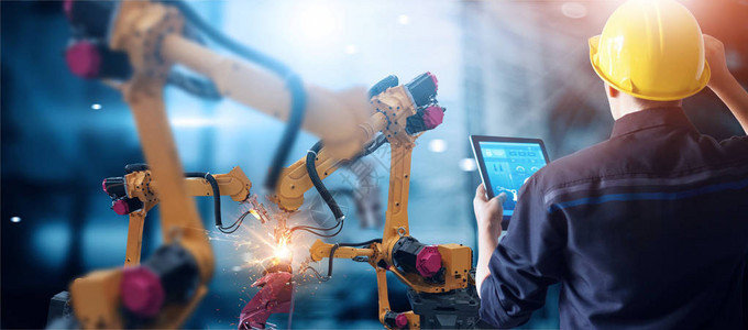 工程师用监控系统软件检查和控制智能工厂汽车工业中的焊接机器人自动臂机数字制造业务工业40背景图片
