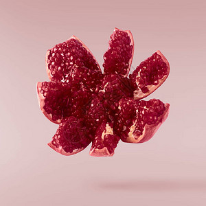 在空气中飞翔，新鲜成熟的石榴分离在粉红色的背景上。高分辨率图像图片