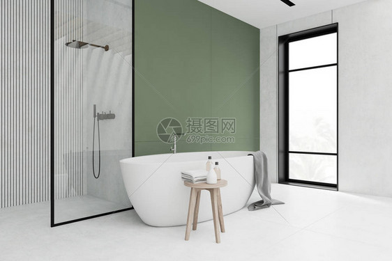 时尚浴室的角落有绿色和白色的墙壁瓷砖地板舒适的浴缸和挂着毛巾的浴缸带产品和毛巾的架子以及玻璃墙淋浴间图片