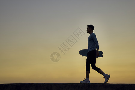 夕阳下男青年拿着滑板行走的剪影图片