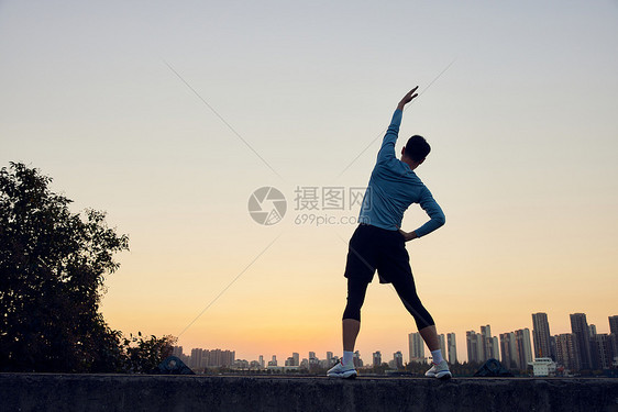 夕阳下男青年运动拉伸背影图片