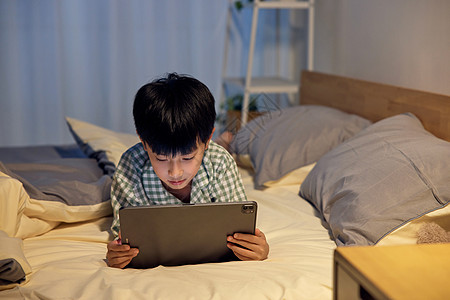 夜晚在床上玩平板电脑的小男孩图片