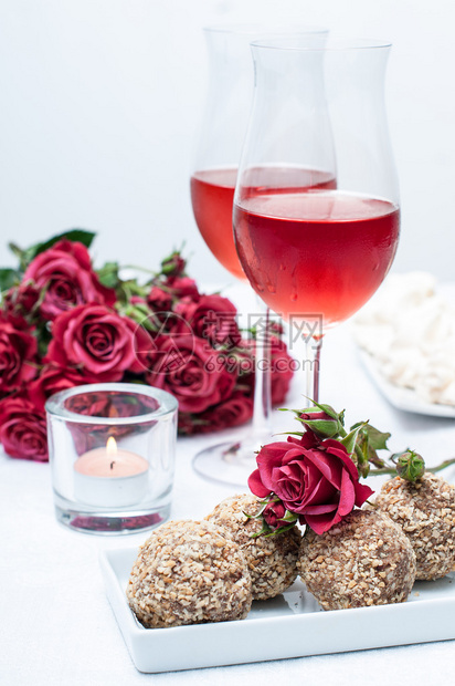 两杯玫瑰红酒新鲜花蛋糕和零食在节日餐桌图片