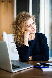 一位年轻女在现代室内坐在便携式笔记本电脑前思图片