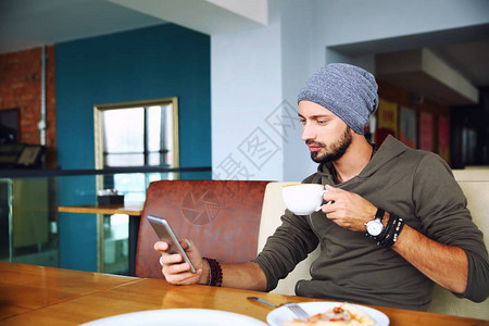 年轻帅气的时装男长着胡子坐在咖啡馆里说着手图片