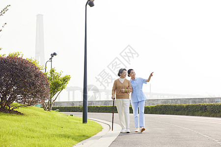 老人散步年轻女护工陪伴老人公园散步背景
