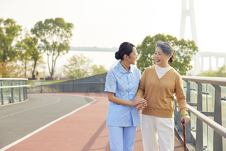 照顾老人年轻女护工户外陪伴老人散步背景