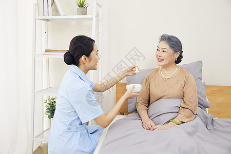 照顾老人年轻女护工给卧床的老奶奶喂食背景