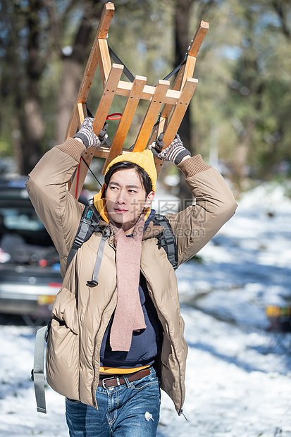 雪地上步行举着雪橇的青年男人图片