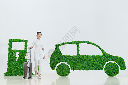 电动环保商务女士推着行李箱走在电动汽车旁背景