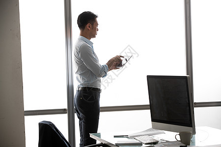商务男士在窗户前使用平板电脑图片