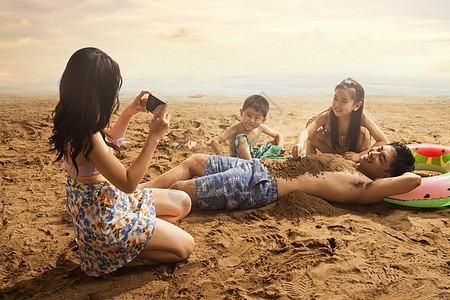 沙滩上青年女人为丈夫孩子拍照图片