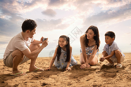 沙滩上青年男人为妻子孩子拍照图片