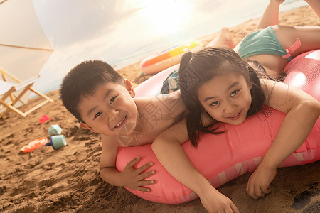 沙滩上的快乐东方儿童趴在游泳圈上玩耍图片