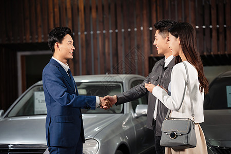 汽车销售人员和青年夫妇握手背景