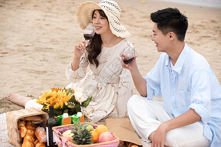 浪漫的青年夫妇坐在沙滩上喝红酒图片