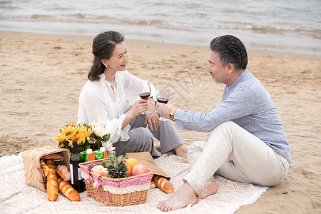 幸福的老年夫妇坐在海滩上野餐饮酒图片