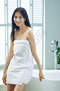 裹着浴巾的青年女人站在浴缸旁图片