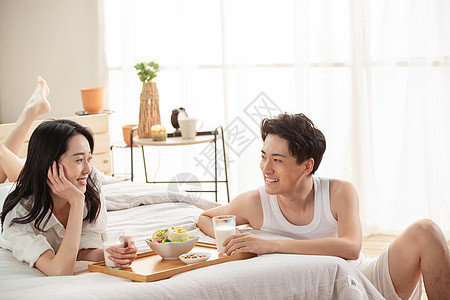 快乐的年轻情侣在床上吃早餐图片