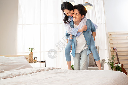 卧室内年轻的丈夫背着妻子放松高清图片素材