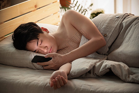 躺在床上玩手机的年轻男人图片