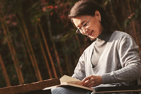 户外老年女人坐在轮椅上看书图片