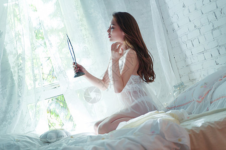 自信的青年女人坐在床上照镜子图片
