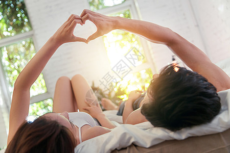 山顶阳光幸福的年轻伴侣躺在床上做心形手势背景