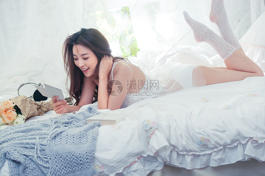 趴在床上欣赏明信片的青年女人图片