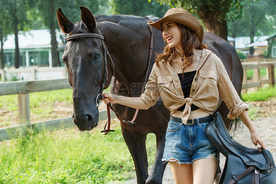 马场内快乐的青年女人拿着马具牵着马图片