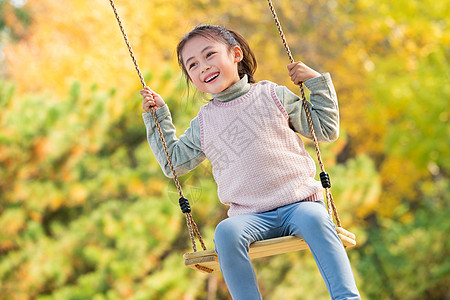 小孩嬉戏快乐的小女孩在公园里荡秋千背景