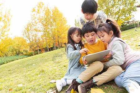 四个小朋友坐在草地上看平板电脑图片