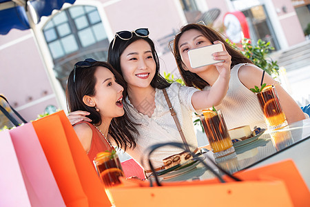年轻女孩们坐在路边咖啡馆拿手机自拍图片