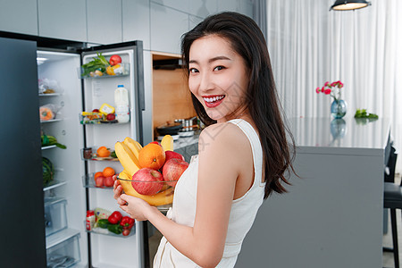 拿着水果的青年女人站在冰箱前图片