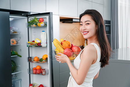 拿着水果的青年女人站在冰箱前图片