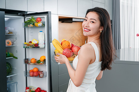 拿着水果的青年女人站在冰箱前图片