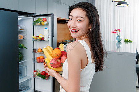 拿着水果的青年女人站在冰箱前图片