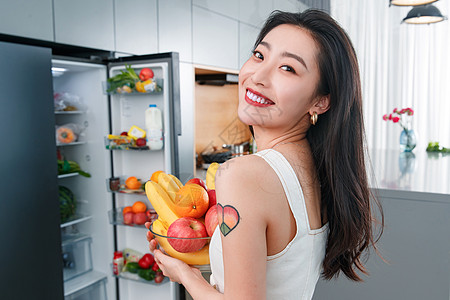 拿着水果的青年女人站在冰箱前图片