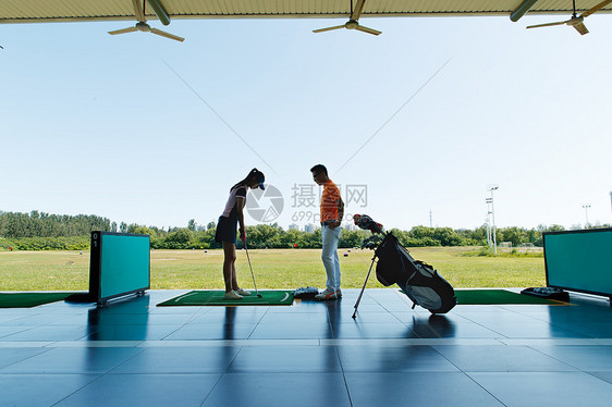 练习场上教练指导青年女人打高尔夫图片
