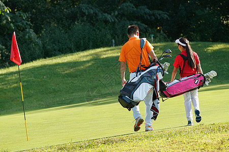 球场上教练和学生背着高尔夫球包步行的背影图片