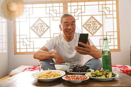 老人吃老年人坐在家里吃饭看手机背景
