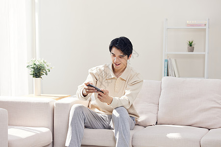 坐在客厅的年轻人使用手机玩游戏图片